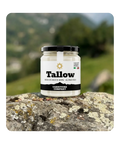Barattolo di vetro con tappo nero di Tallow - sego di Angus 100% al pascolo di Carnivore Company, posato su roccia con licheni e sfondo verde montagna